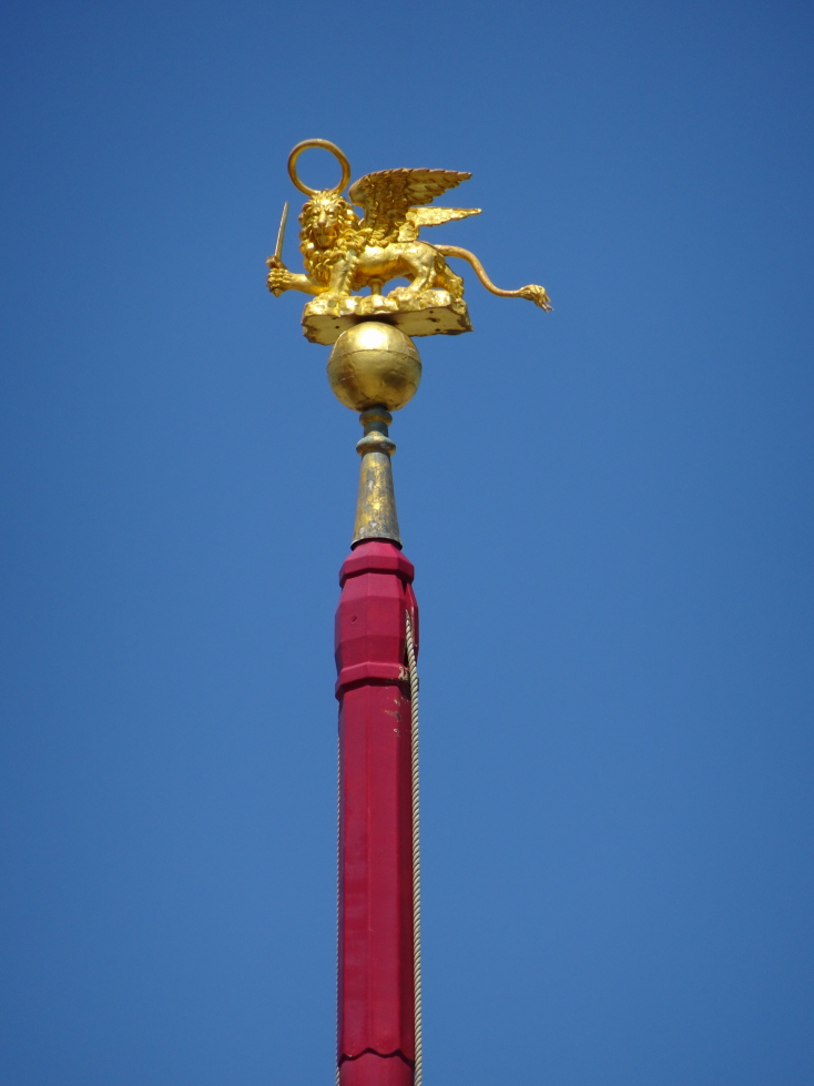 Golden winged lion atop a tall red flag pole Piazza San Marco